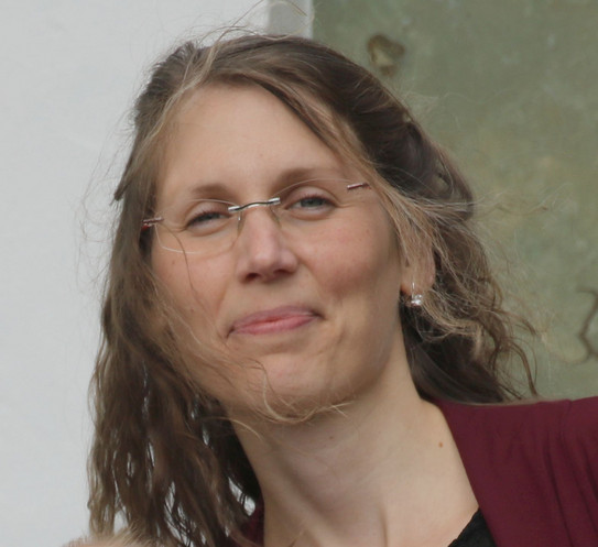 Portraitfoto von Christina Ringel (weiblich, lächelnd, lange braune im Wind wehende Haare, Brille)