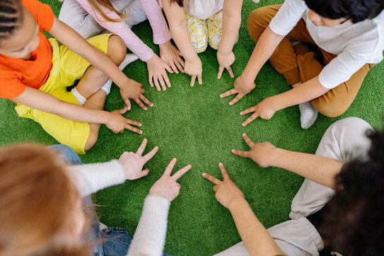 Kinder sitzen im Kreis und halten die Hände in die Mitte