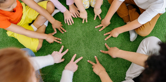 Kinder sitzen im Kreis und halten die Hände in die Mitte