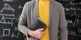 Lehrer mit Buch in der Hand vor Tafel