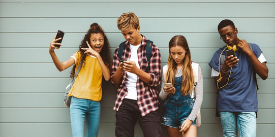 vier Schüler*innen stehen nebeneinander und schauen auf ihre Smartphones