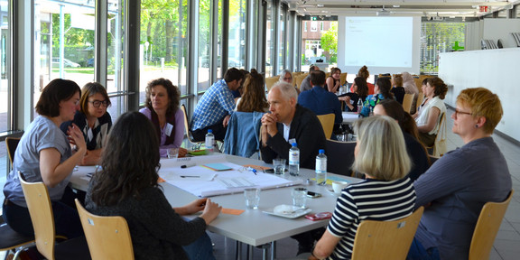 viele Personen sitzen an Tischgruppen und diskutieren miteinander.