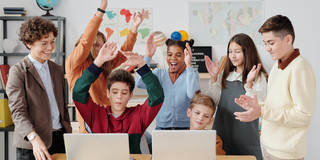 Mehrere Schüler*innen sitzen vor Laptops. Eine Lehrerin steht daneben.