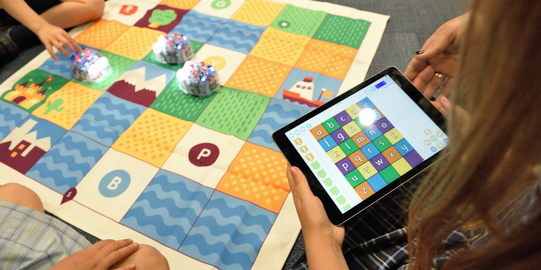 Person mit Tablet in der Hand vor einem Spielbrett