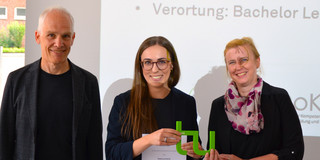 drei Personen schauen in die Kamera und stehen vor einer Leinwand