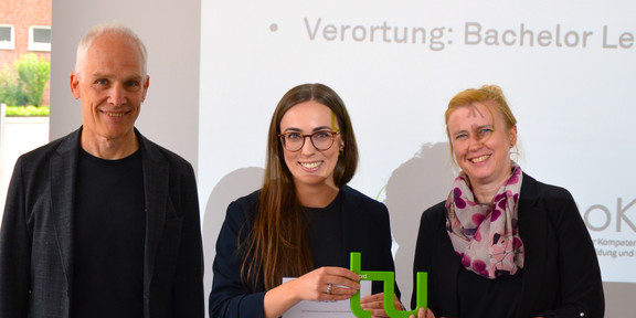 drei Personen schauen in die Kamera und stehen vor einer Leinwand