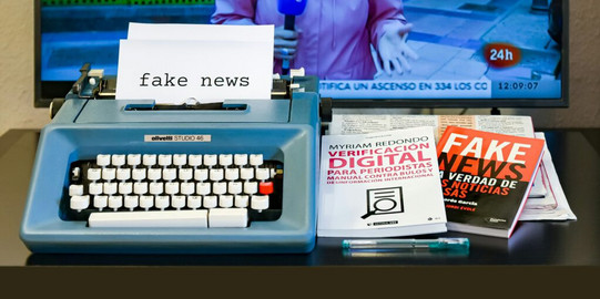 alte Schreibmaschine mit Zettel auf dem Fake News steht und Bücher