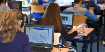Personen sitzen an Tischen und arbeiten an Laptops