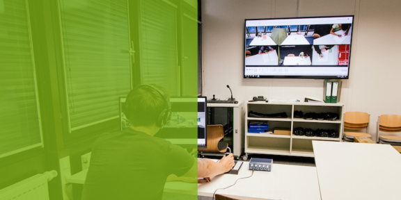 Foto eines Raums mit mehreren Tischen, Stühlen und technischer Ausstattung. Eine Person sitzt mit Kopfhörern an einem Tisch und bedient ein Audiogerät. Im Hintergrund zeigt ein Bildschirm mehrere Videoaufnahmen. Die linke Bildhälfte ist grün eingefärbt und trägt die Aufschrift „Tag der offenen Tür“.