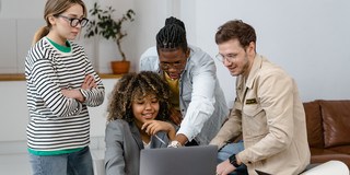 Vier Studierende stehen bzw. sitzen an einem am Laptop