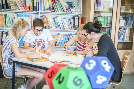 Vier Personen sitzen in der Mathedidaktik-Werkstatt am Tisch und bauen mit Würfeln.