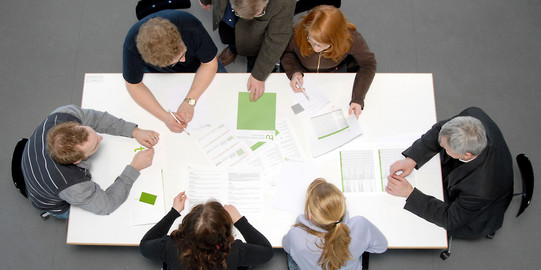 Besprechungssituation Studenten und Professoren Studierende und Dozierende sitzen gemeinsam an einem Tisch und arbeiten.