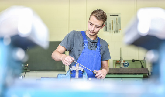 Ein Auszubildender zum Industriemechaniker feilt an einem metallischen Gegenstand.